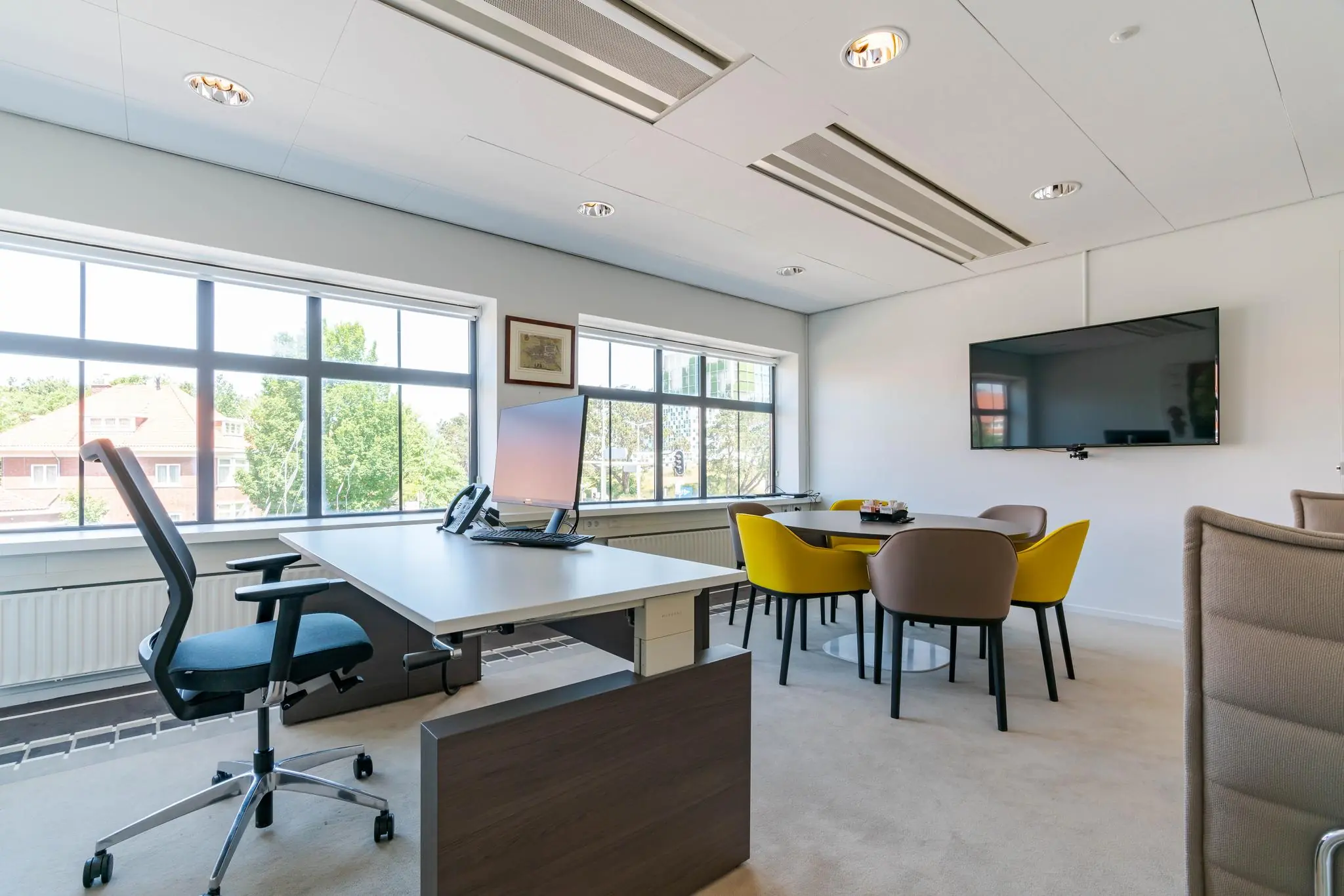 Modern kantoor aan de Van Alkemadelaan met werkplek, vergadertafel en grote ramen die uitzicht bieden op een groene omgeving.